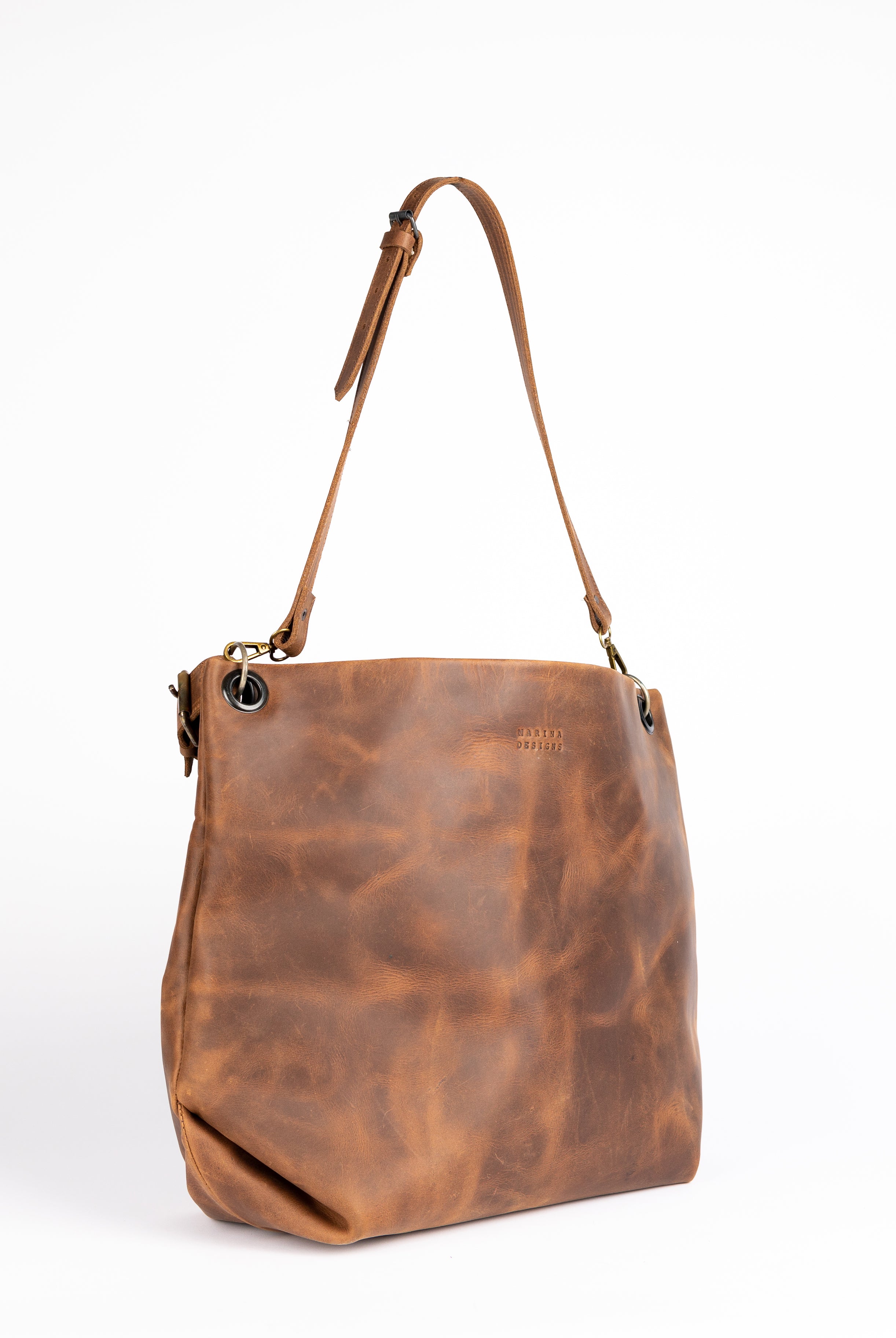 Angled view showcasing the bag’s structured form and gentle slouch at the base, emphasizing the natural texture and artisanal finish of the castano leather. The leather strap and grommet detail enhance its refined look.