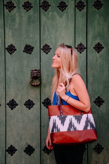 Kendra carrying a Husky leather and woven textile tote beside a green door