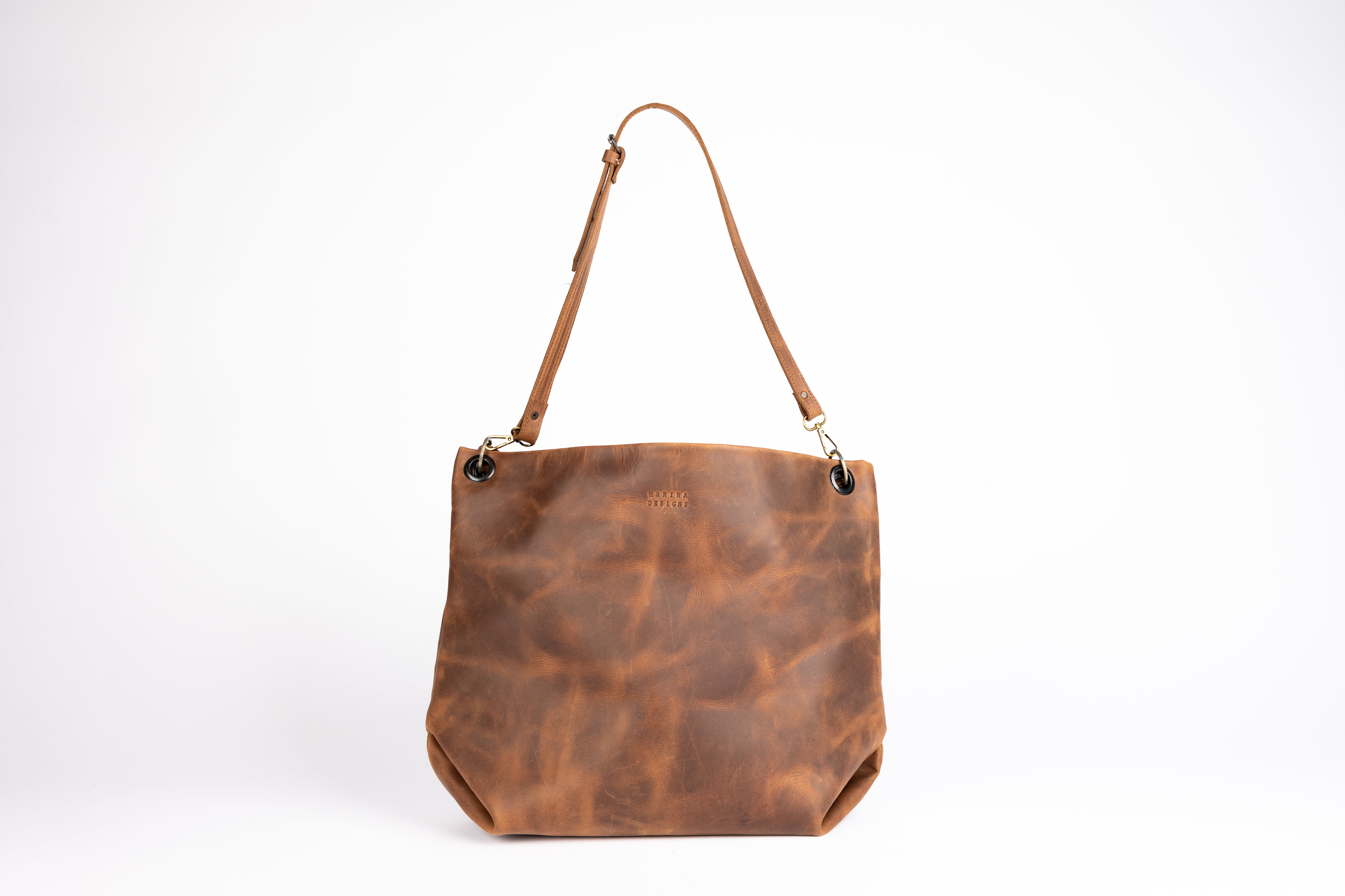  Straight-on view of the Parisian Tote, highlighting its smooth, full-grain castano leather and elegant minimalist shape. The adjustable shoulder strap is shown centered, with brass hardware and grommet details.