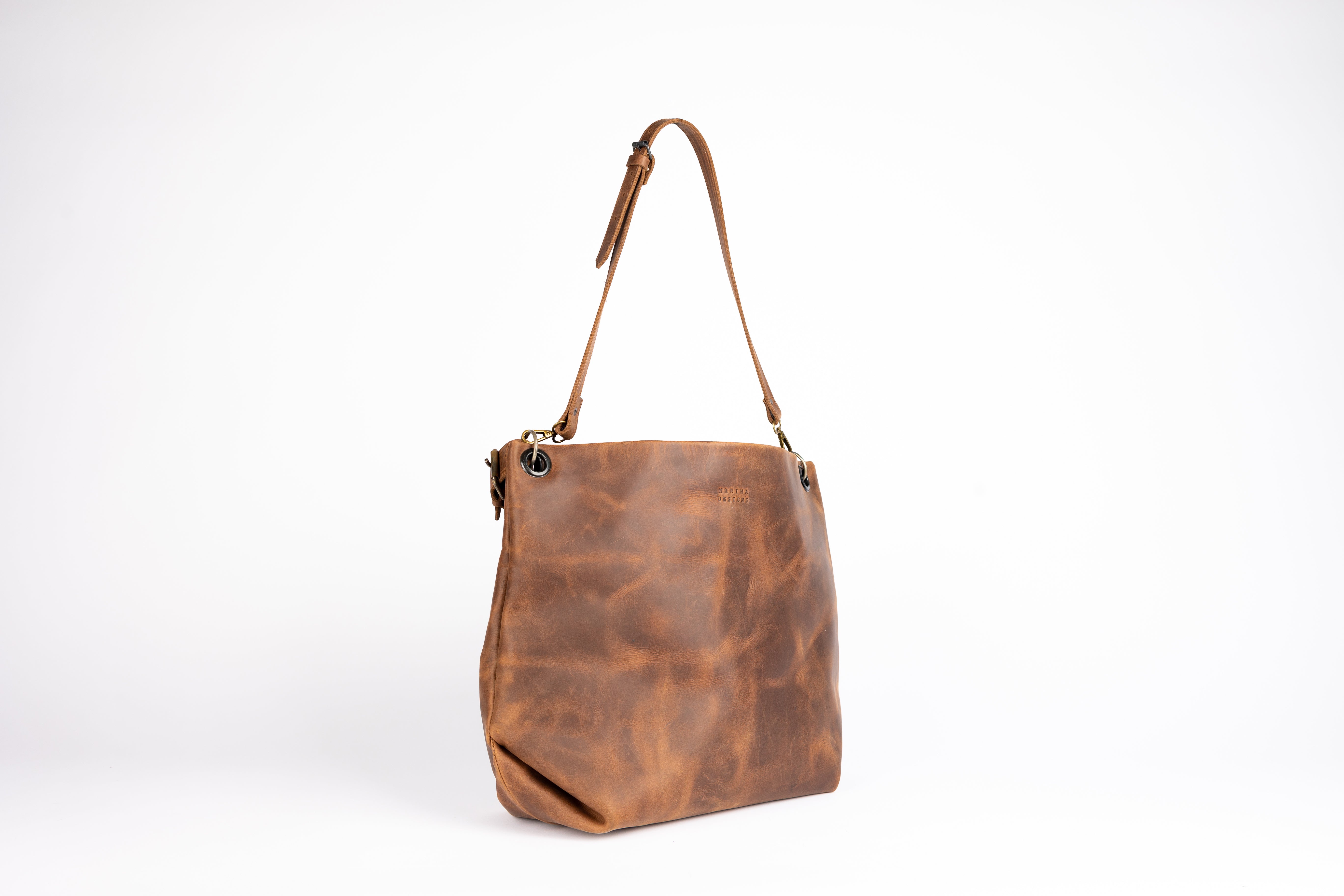 Angled view showcasing the bag’s structured form and gentle slouch at the base, emphasizing the natural texture and artisanal finish of the castano leather. The leather strap and grommet detail enhance its refined look.
